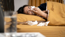 An Asian Woman Lying In Bed Blowing Her Nose With a Tissue Acute Vs Chronic Sinusitis